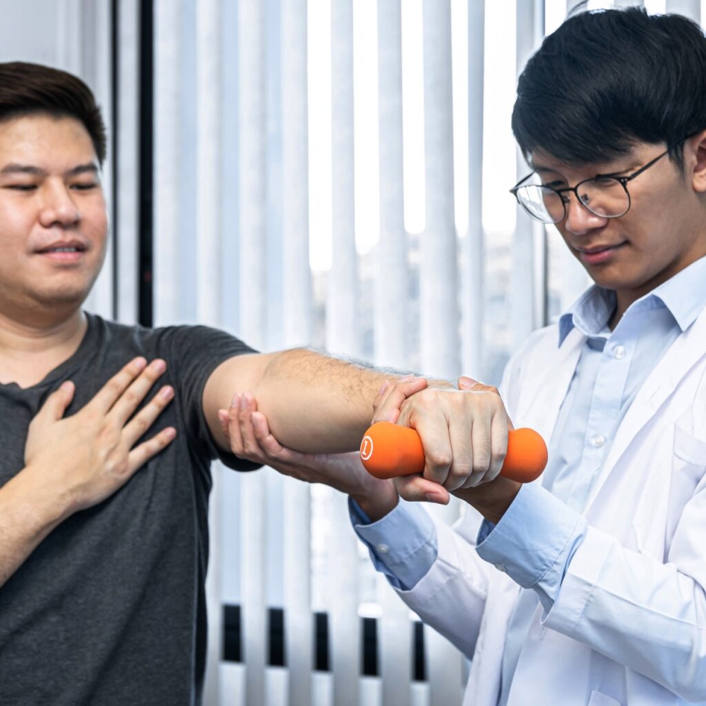 young Asian physiotherapist helping patient stretching arm during exercise