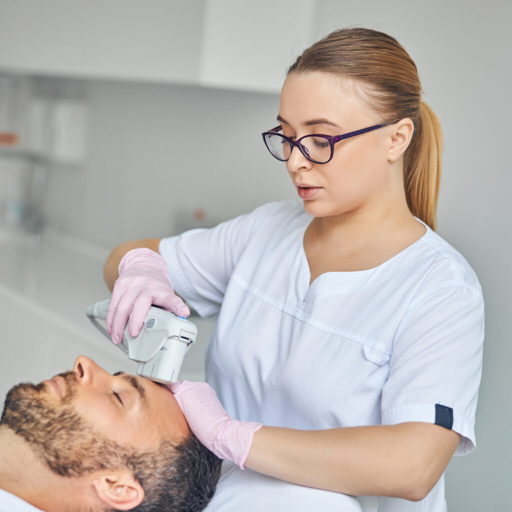 female esthetician treating male skin with laser device