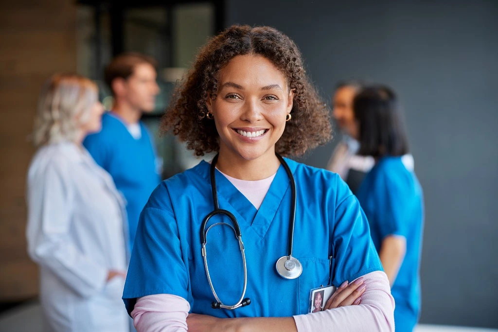 female nurse in blue scrubs smiling confidently, showcasing detail-oriented skills