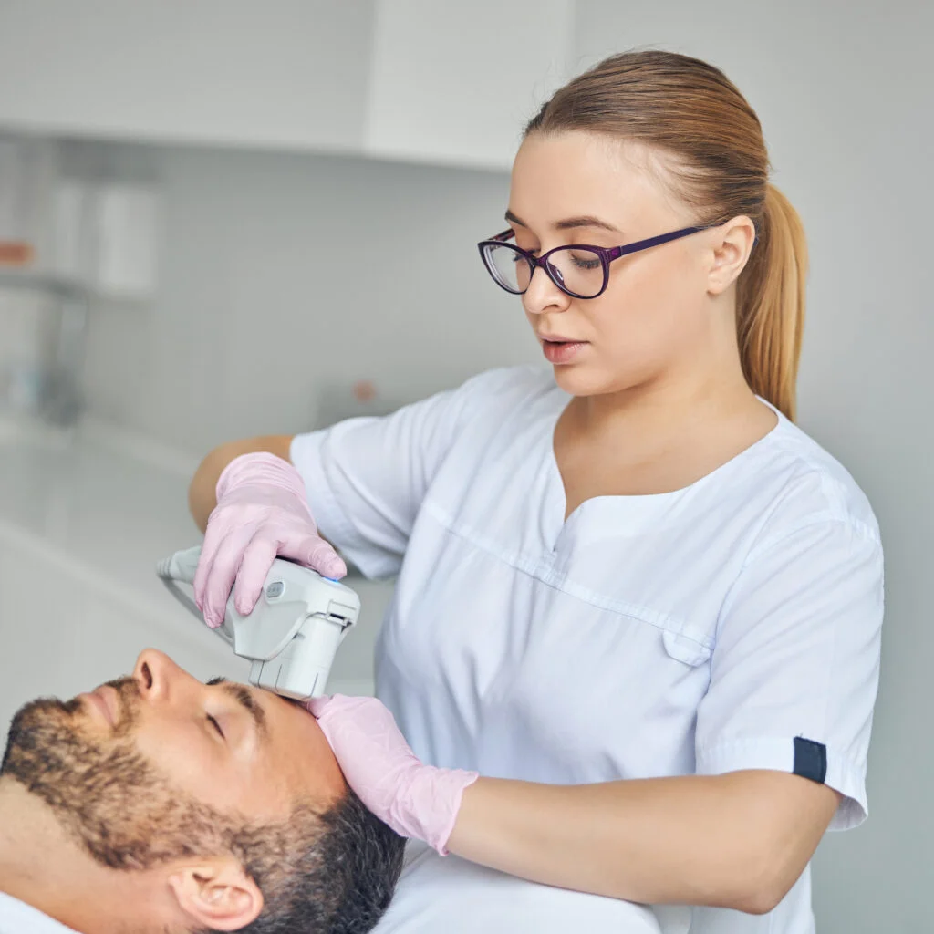 female esthetician treating male skin with laser device